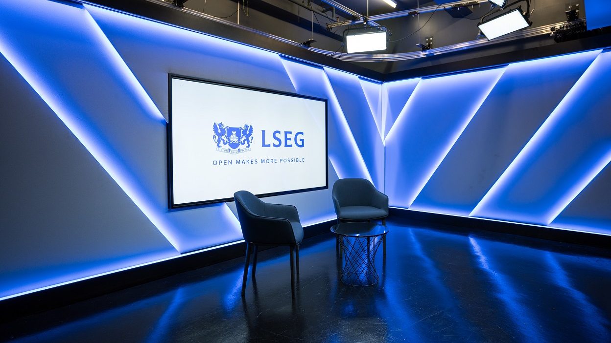 側面から見たスタジオで、小型のガラス製コーヒー・テーブルのまわりに椅子 2 脚を配置。ホストの背後のスクリーンには、「オープンであることでより多くのことを可能に」というキャプション付きの LSEG のロゴ。