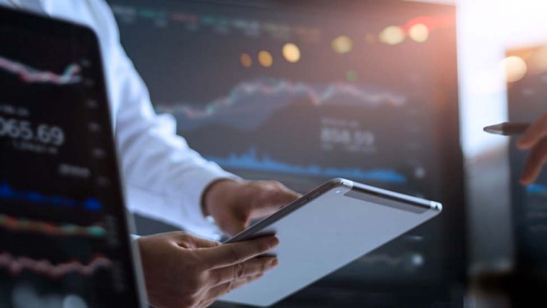 Person using tablet to analyze data with monitors