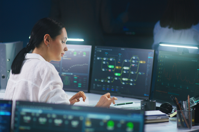 A woman sitting at a desk with multiple screens showing data, charts and graphs.