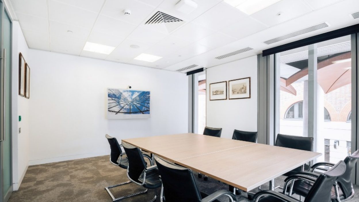 Recess 2 set boardroom table for 8 people facing a small wall ount plasma screen with a sky atrium image