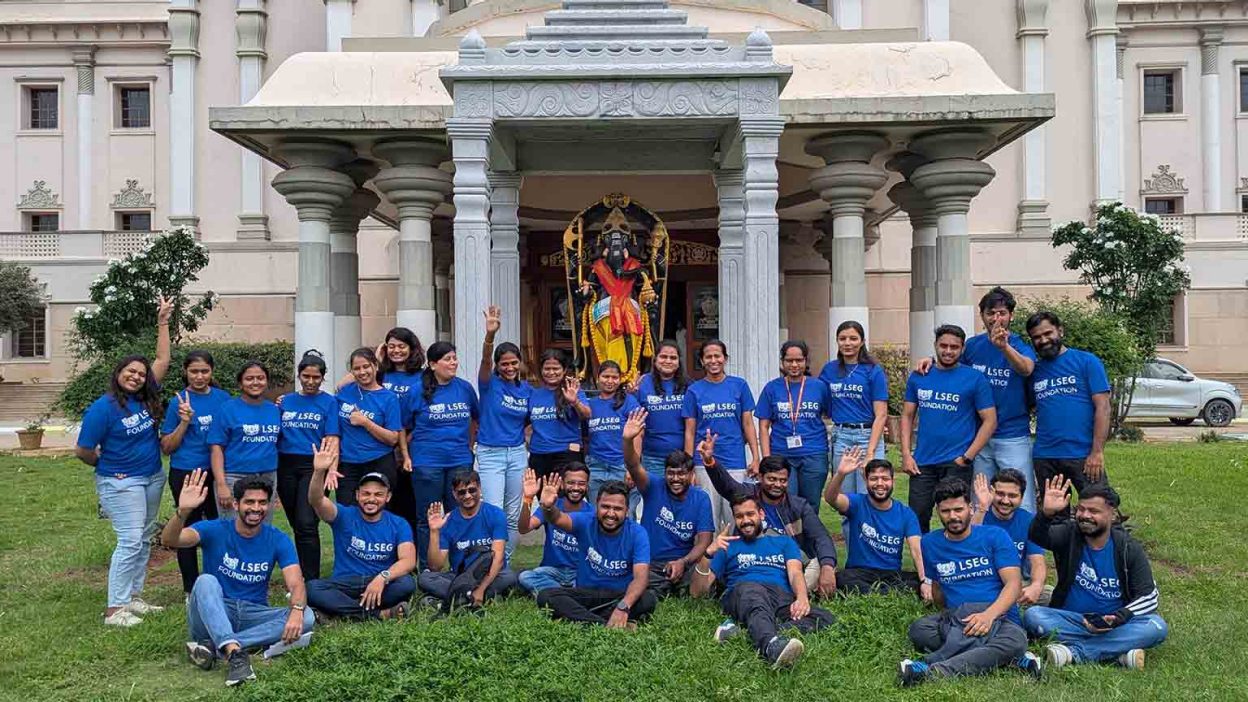 Large group of LSEG volunteers posing together outside Sri Sathya Sai Institute of Medical Sciences Bengaluru, wearing LSEG t-shirts