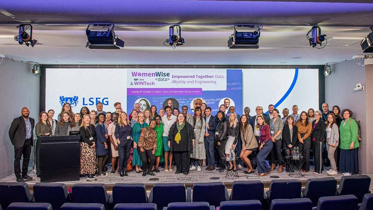 Large group of colleagues gathered on stage for a Women Wise event.