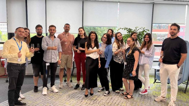 Team members standing together in an office, smiling at the camera.