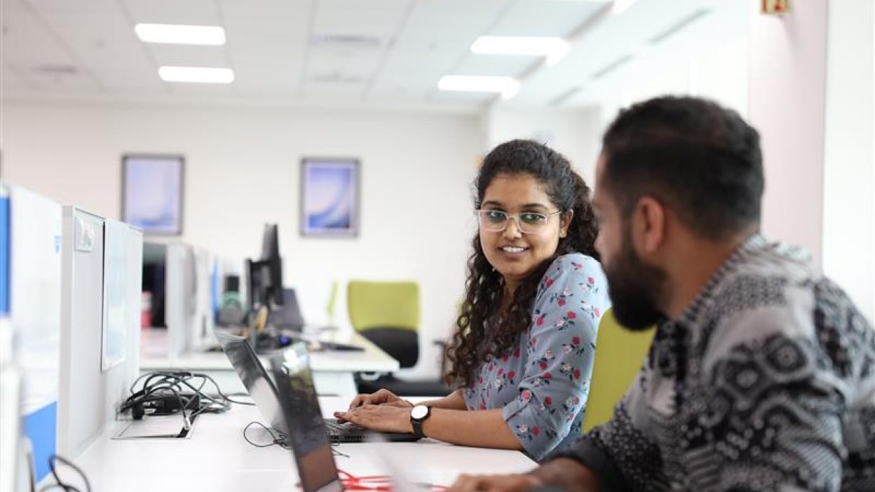 Two colleagues working together at computers in a bright, modern office.